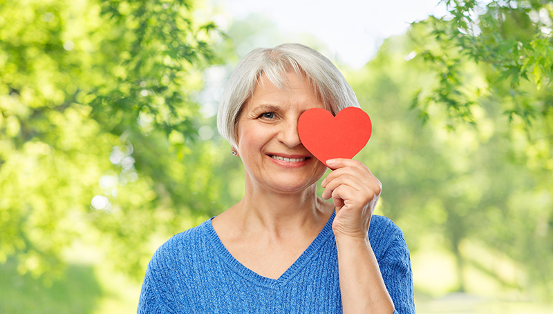 Woman that is smiling and holding a love heart against her eyes