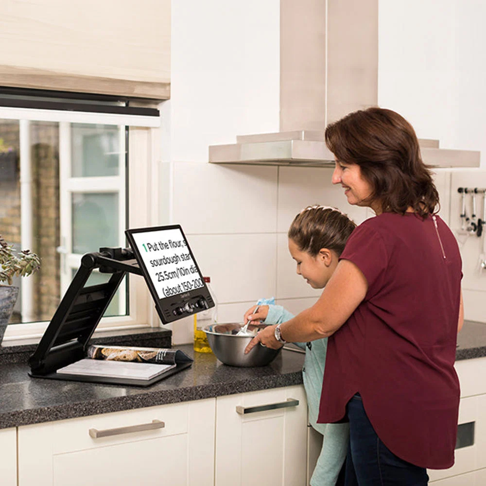 Clearview Go being used in the kitchen ti magnify a recipe by a lady and young girl, possibly her daughter