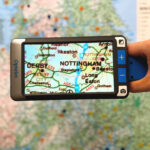 Someone holding the Compact Go by its handle, that is pointed at a UK map, on the screen the areas of Nottingham and Derby are magnified
