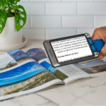 The Compact Go sitting on top of as magazine witht he words enlarged on the Compact Go screen